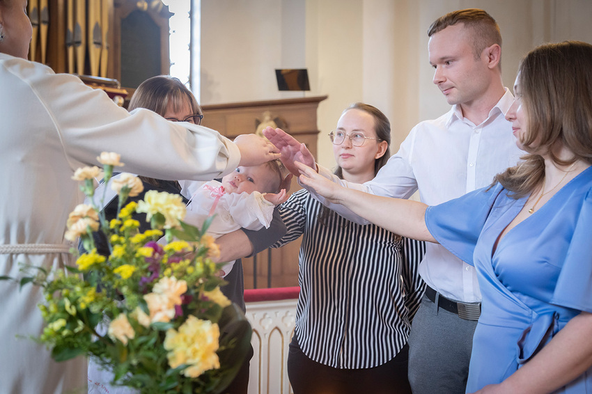 Pieni lapsi aikuisen sylissä. Ympärillä olevat aikuiset pitävät käsiä lapsen pään päällä.